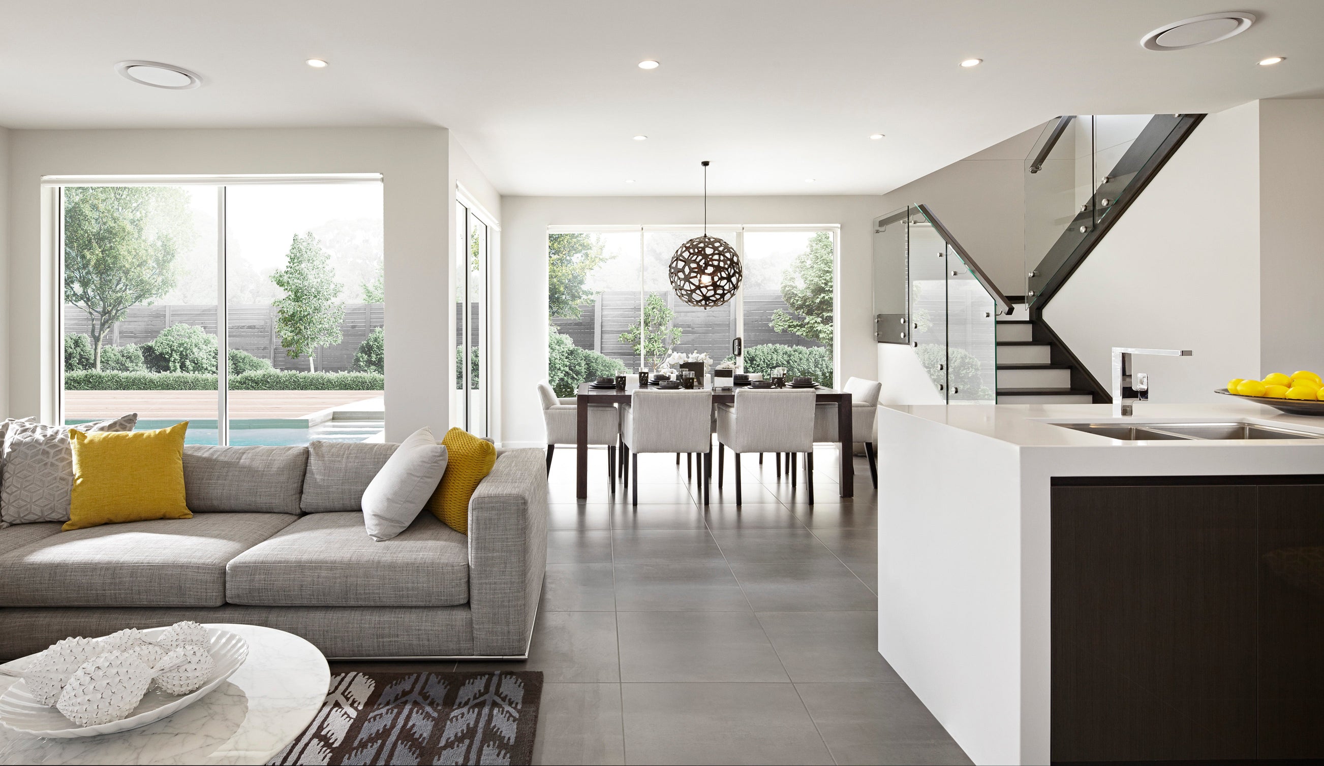 Modern living room with gray sofa, yellow cushions, and a view of a dining area and kitchen.
