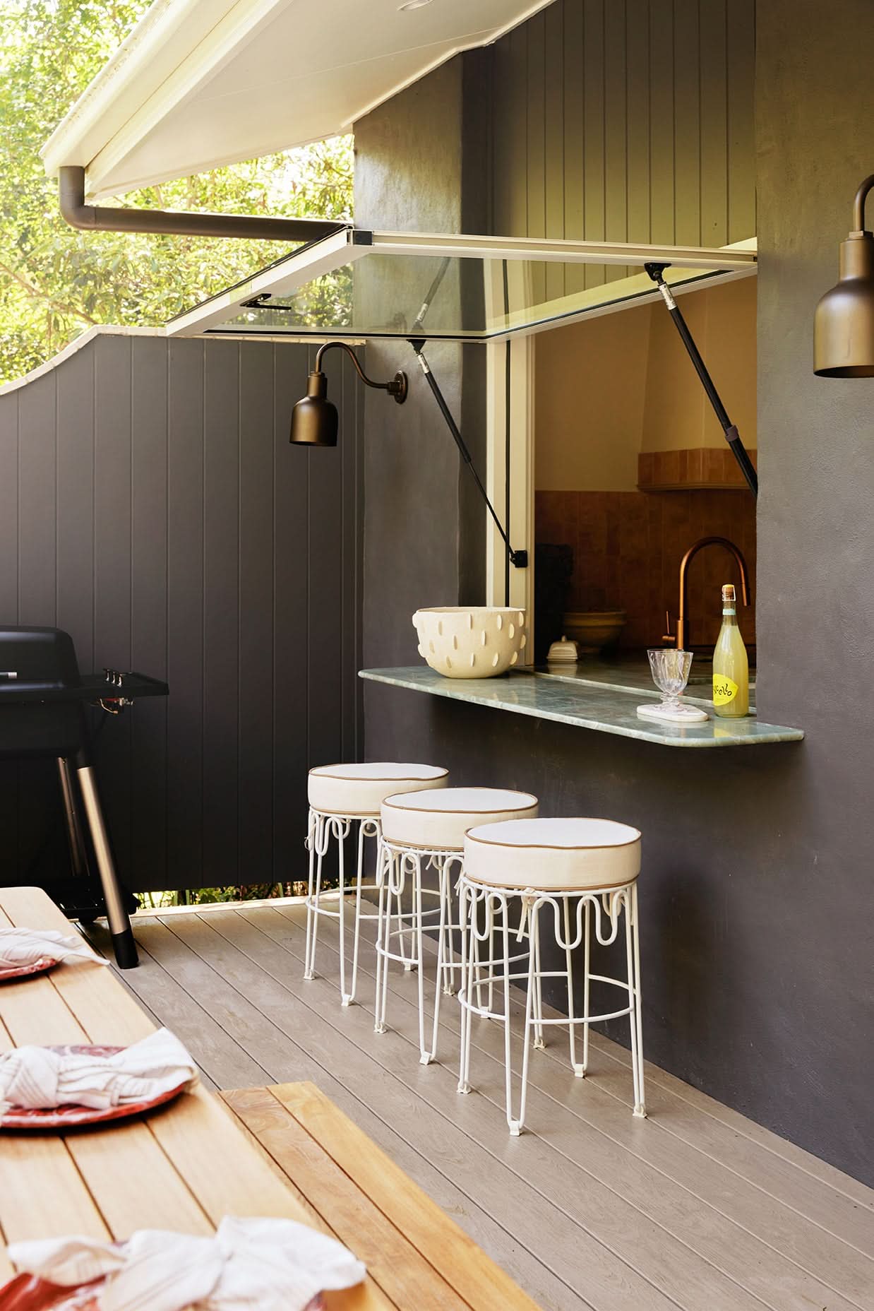 Outdoor patio area with bar stools, a small table, and a wall-mounted shelf.