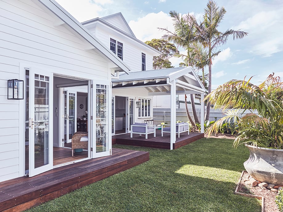 Modern house with open patio, large hinge doors, bi-fold windows, surrounded by greenery and palm trees.