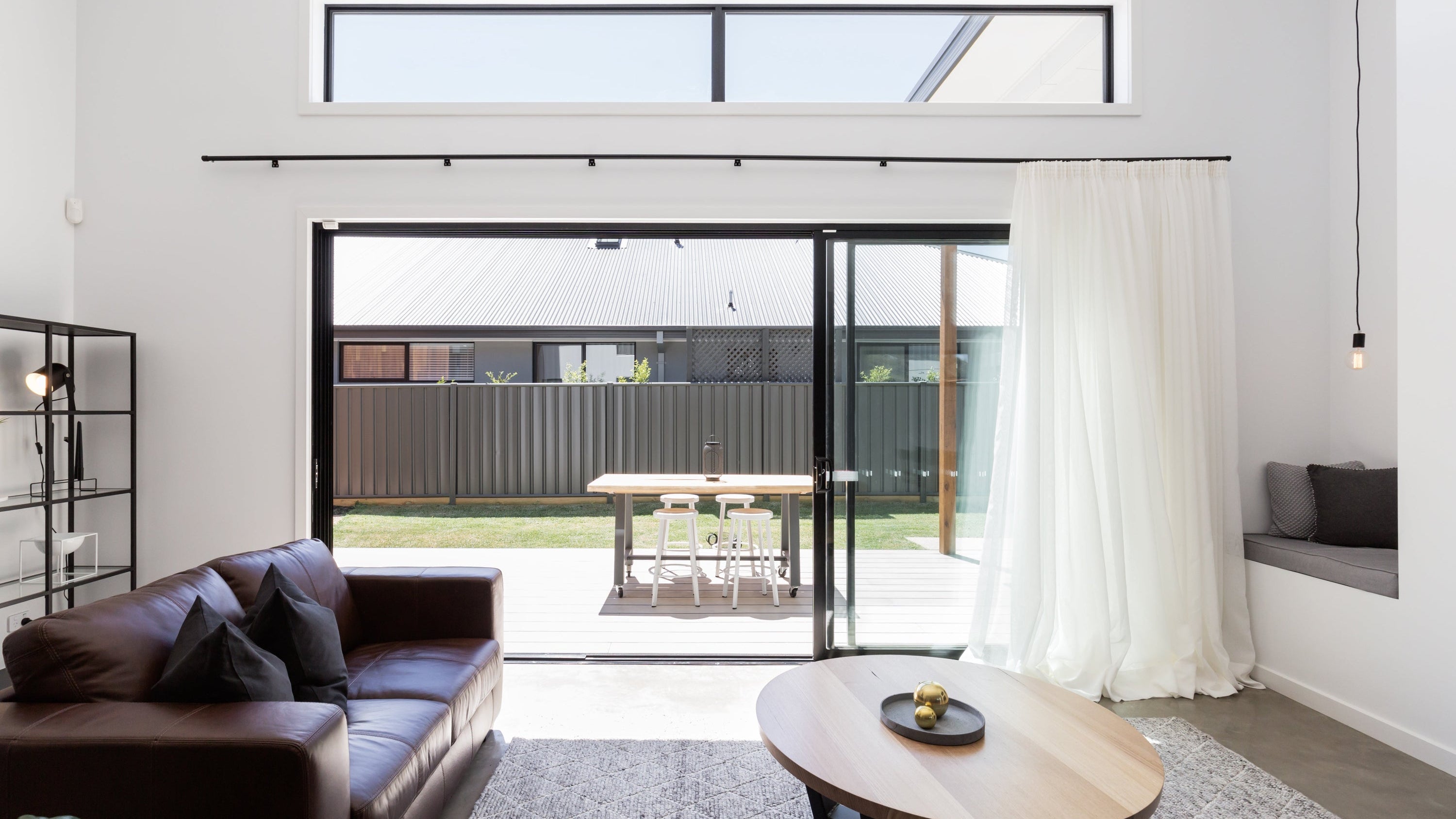 Modern living room with a brown sofa, round wooden coffee table, and large windows.