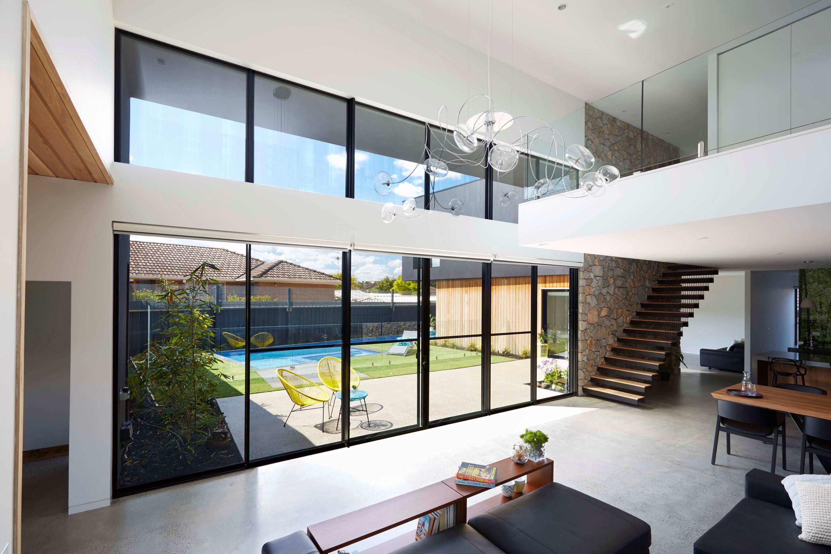 Modern house interior with large glass windows overlooking a pool area.