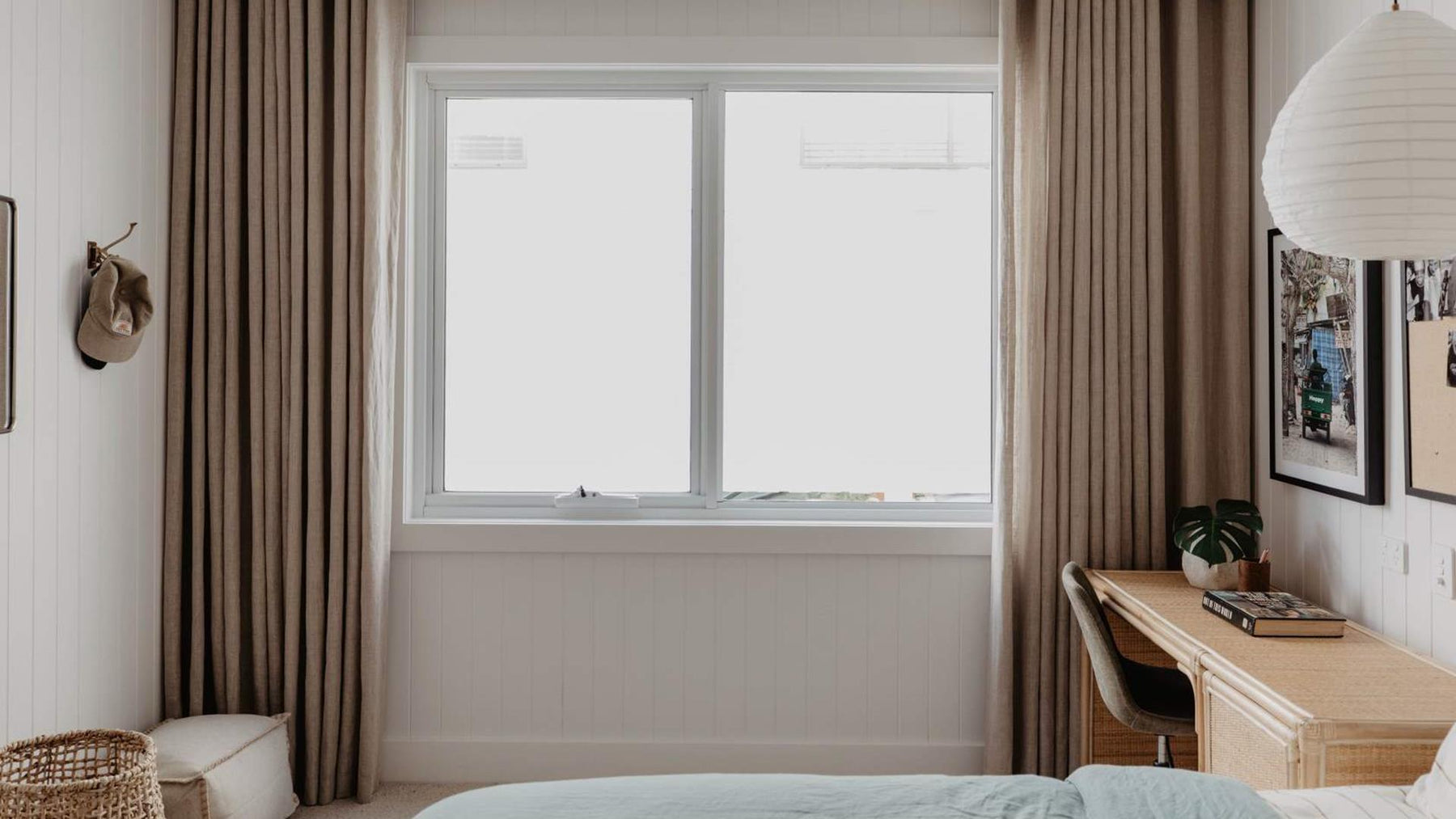 Modern bedroom with a desk, bed, and large window with light brown curtains.