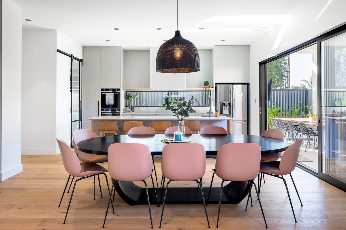 Modern dining area with pink chairs and a round table in a bright kitchen featuring sliding doors.