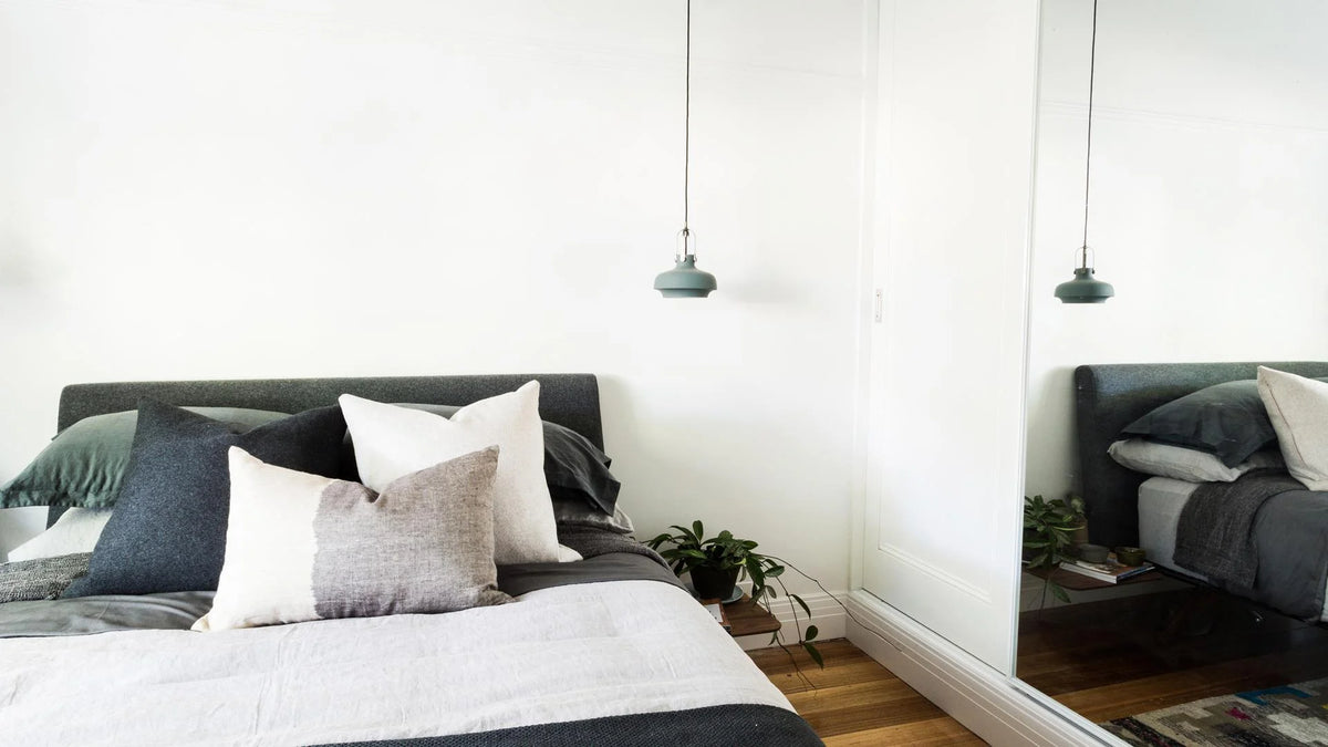Modern bedroom with a bed, pillows, and a framed wardrobe mirror reflecting the room.