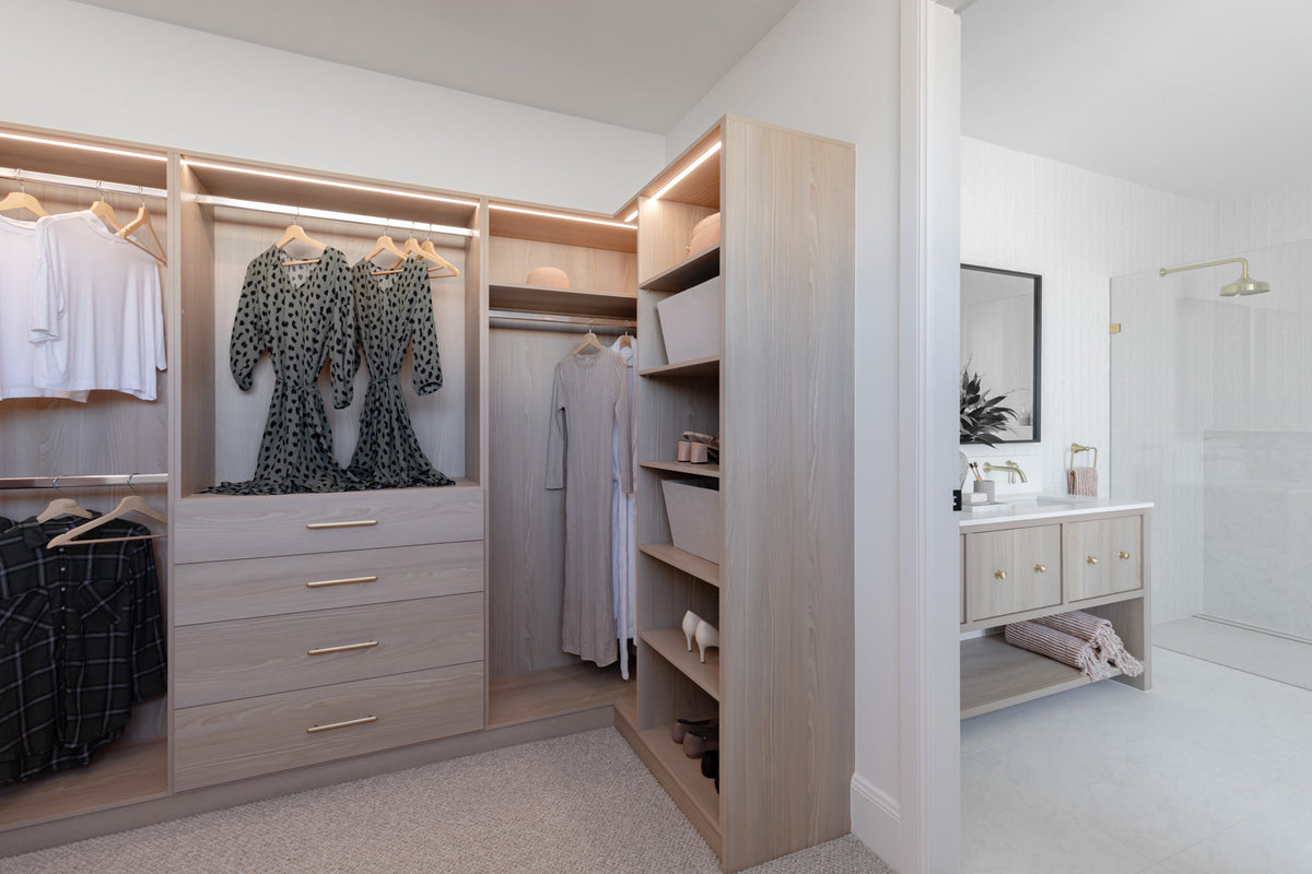 Modern walk-in closet with wooden shelves and drawers in a well-lit room.