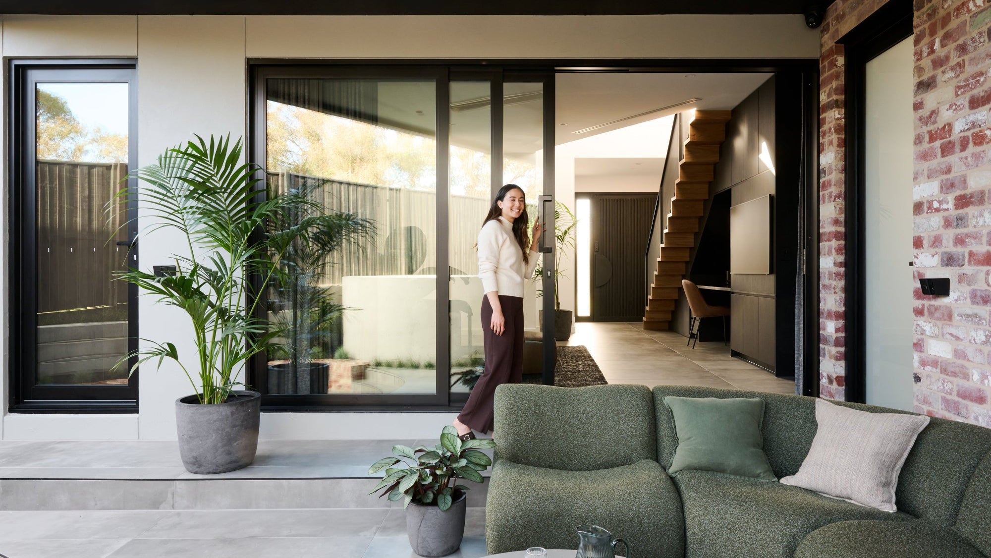 Woman opening exhybrid sliding doors in modern house with a green sofa and plants.