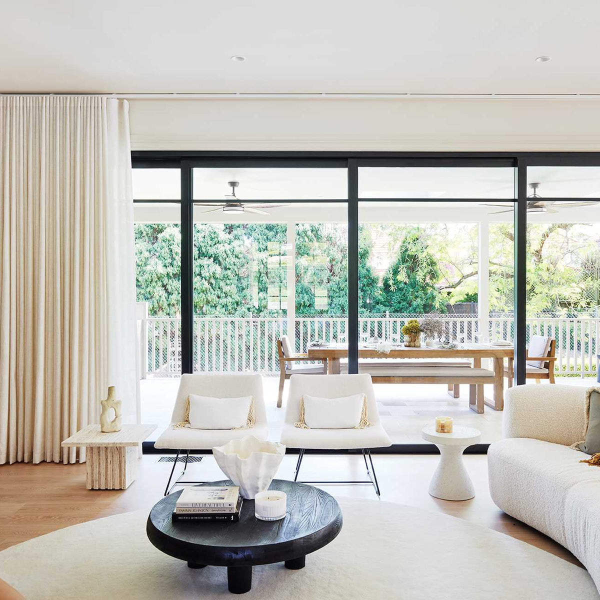 Modern living room with white furniture, large windows, and outdoor view.